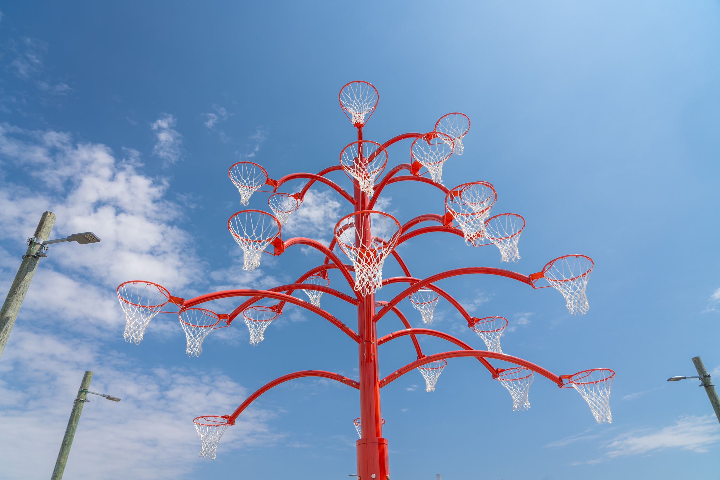 A tall, bright red, tree-like sculpture with multiple basketball hoops on its branches.