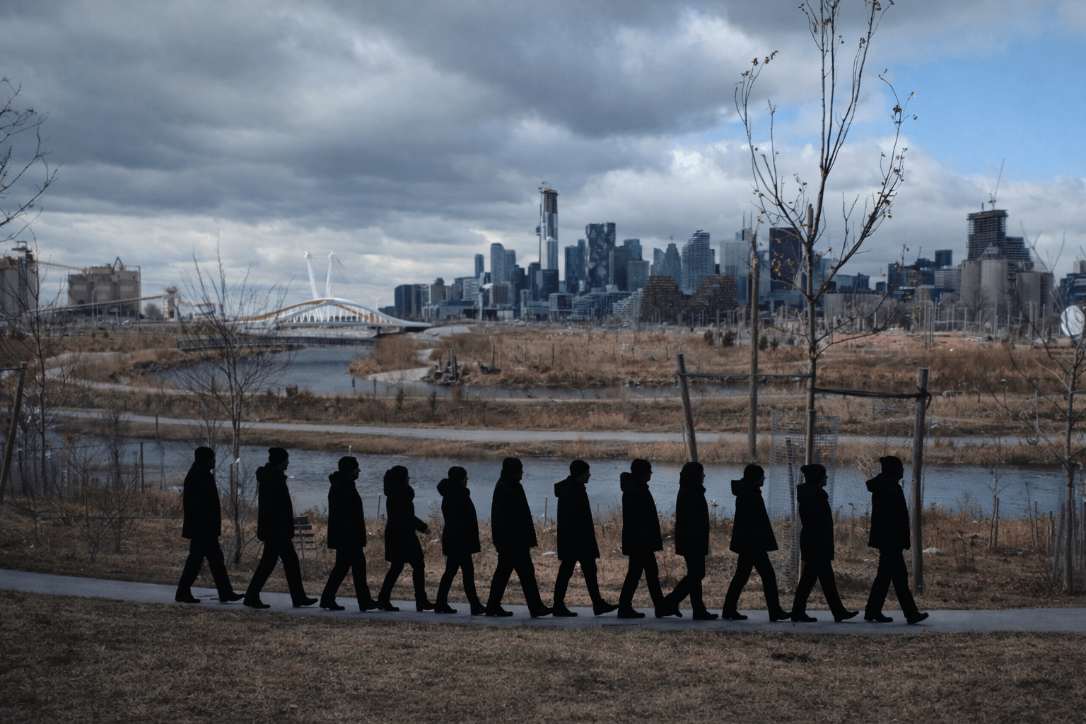 The silhouettes of a procession of people can be seen walking along the river bank