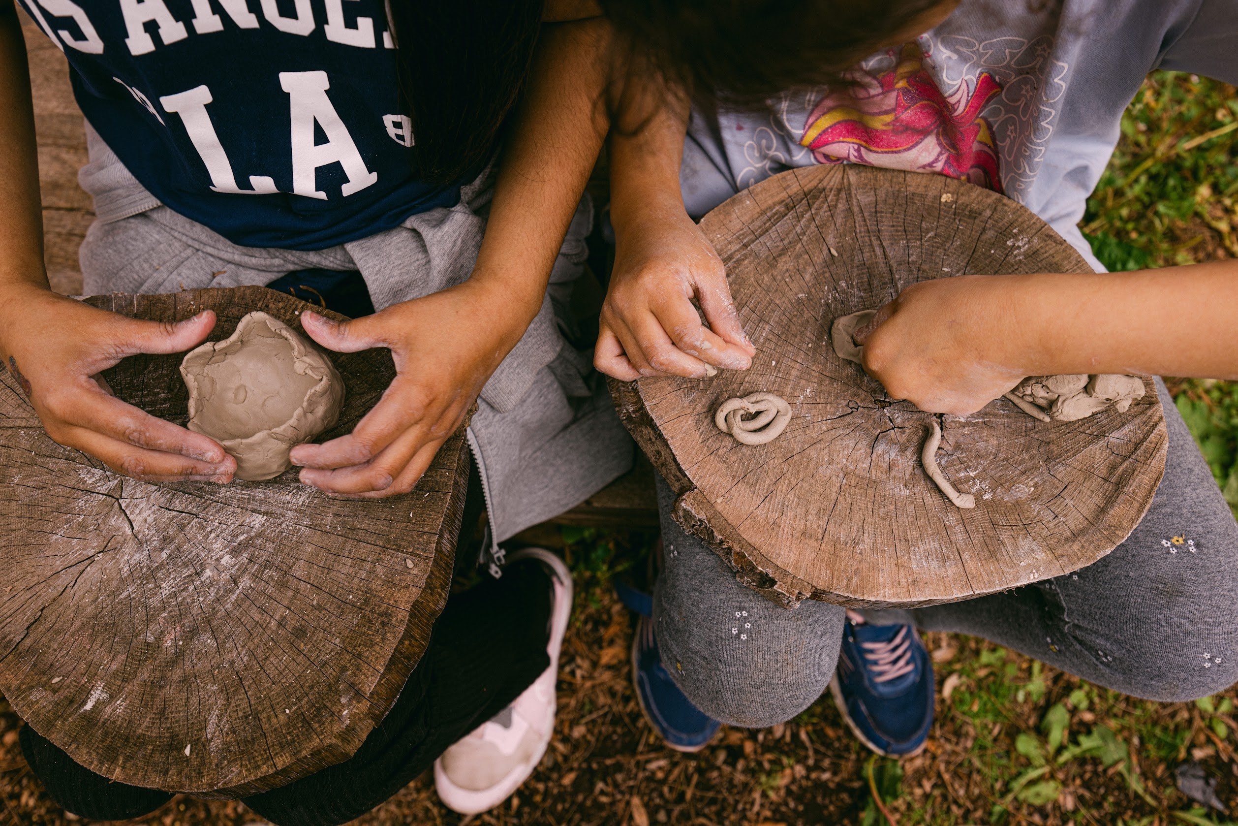 Chidren's hands shaping small clay sculptures atop log slabs