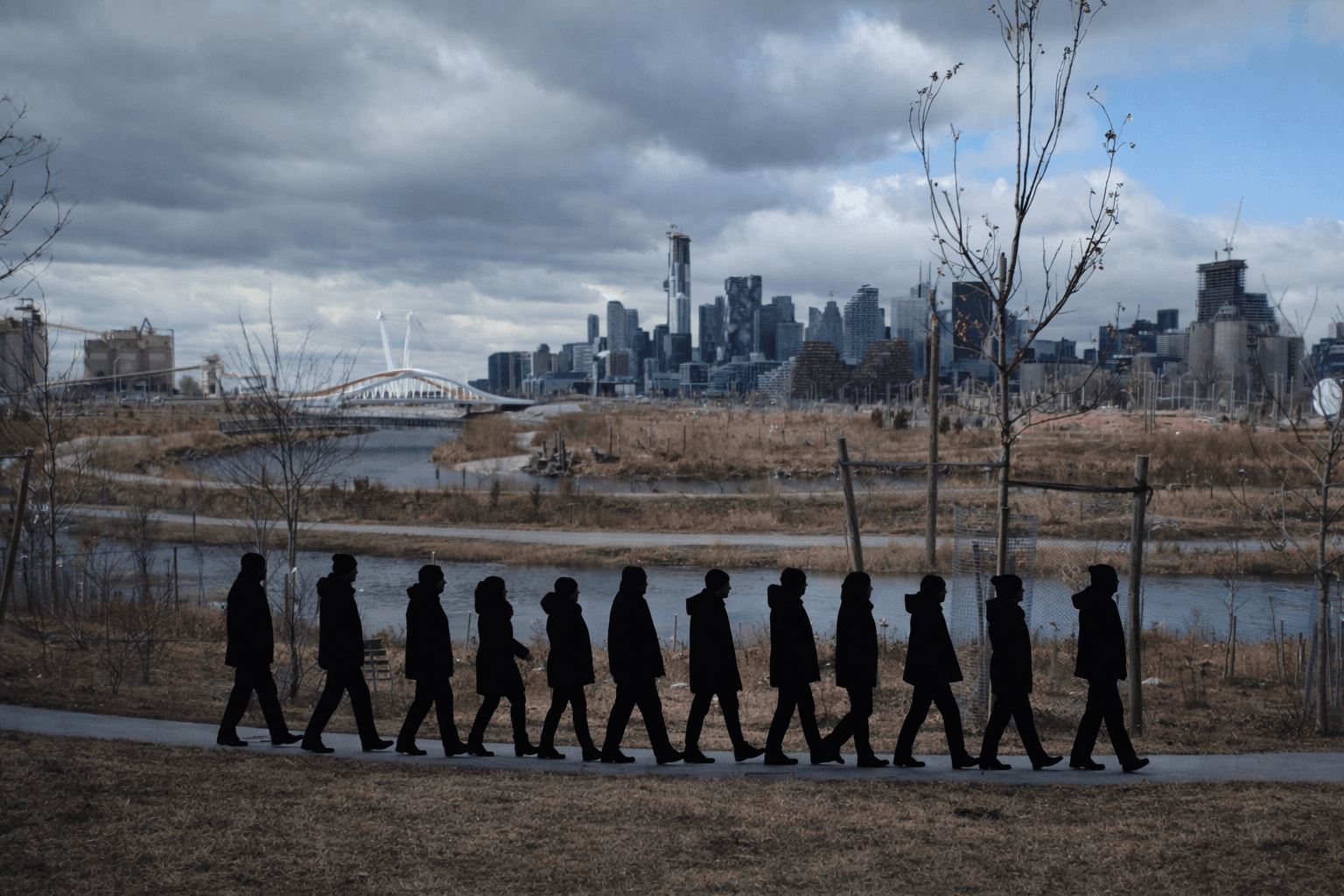 The silhouettes of a procession of people can be seen walking along the river bank